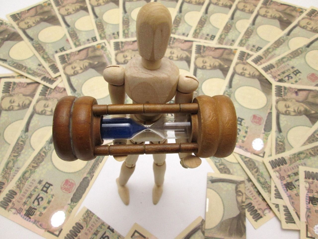 木型の人が砂時計を持ち、日本紙幣に囲まれている写真